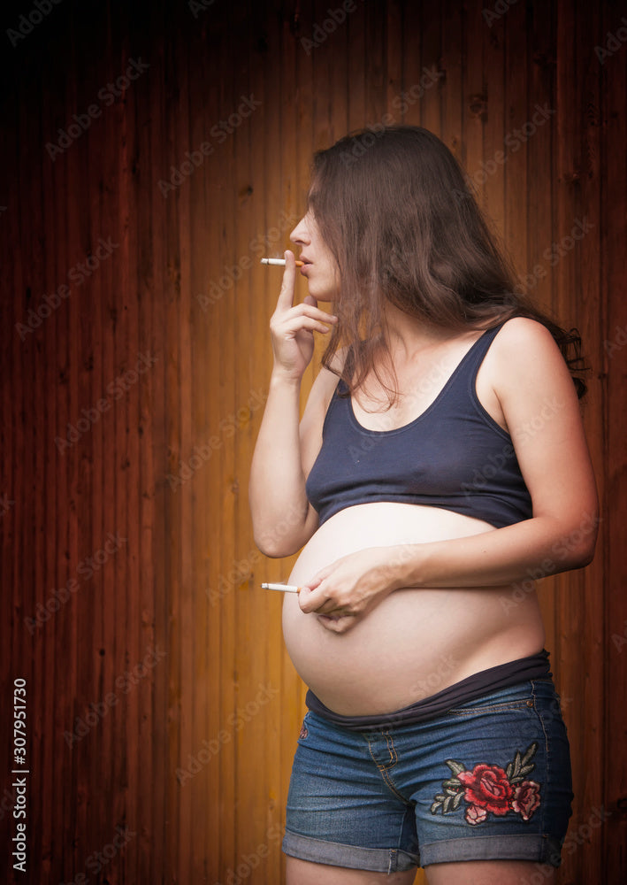 Pregnant smokes cigarettes. Second hand with cigarette near navel/belly.  This symbolizes the impact of cigarettes on the baby Stock-bilde