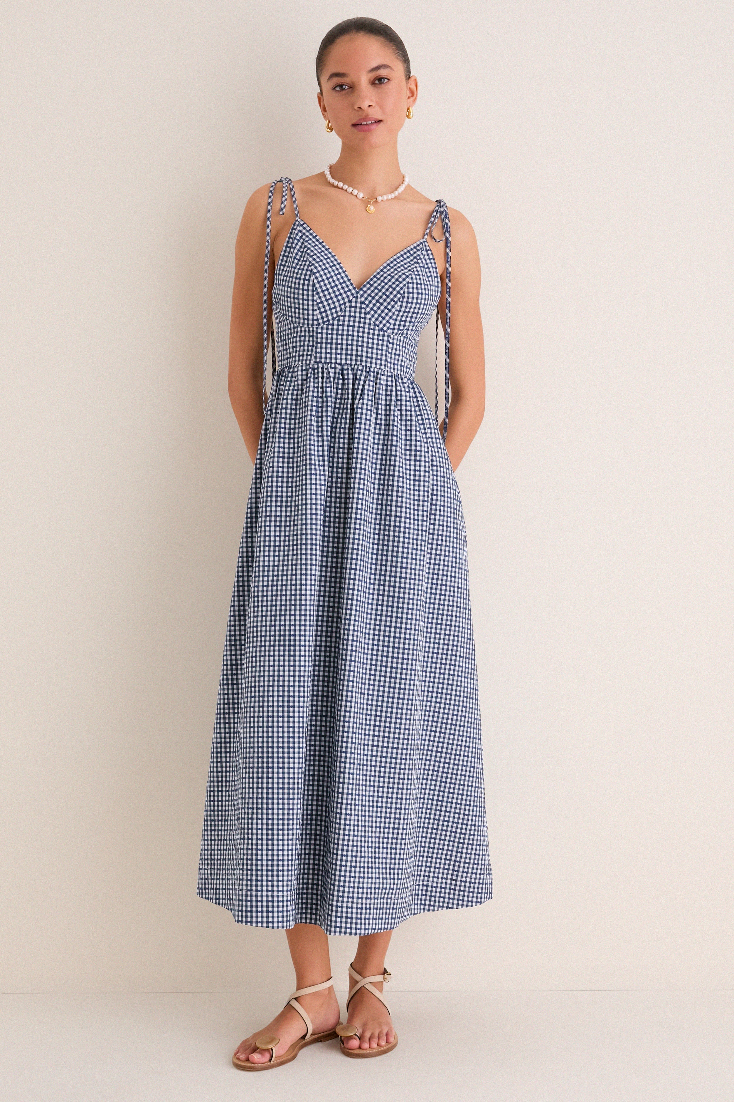 Navy Gingham Sloan Maxi Dress: Effortless and classic, this sleeveless sundress features a V-neck, tie straps, and smocked back, styled with pearl necklace and tan sandals.