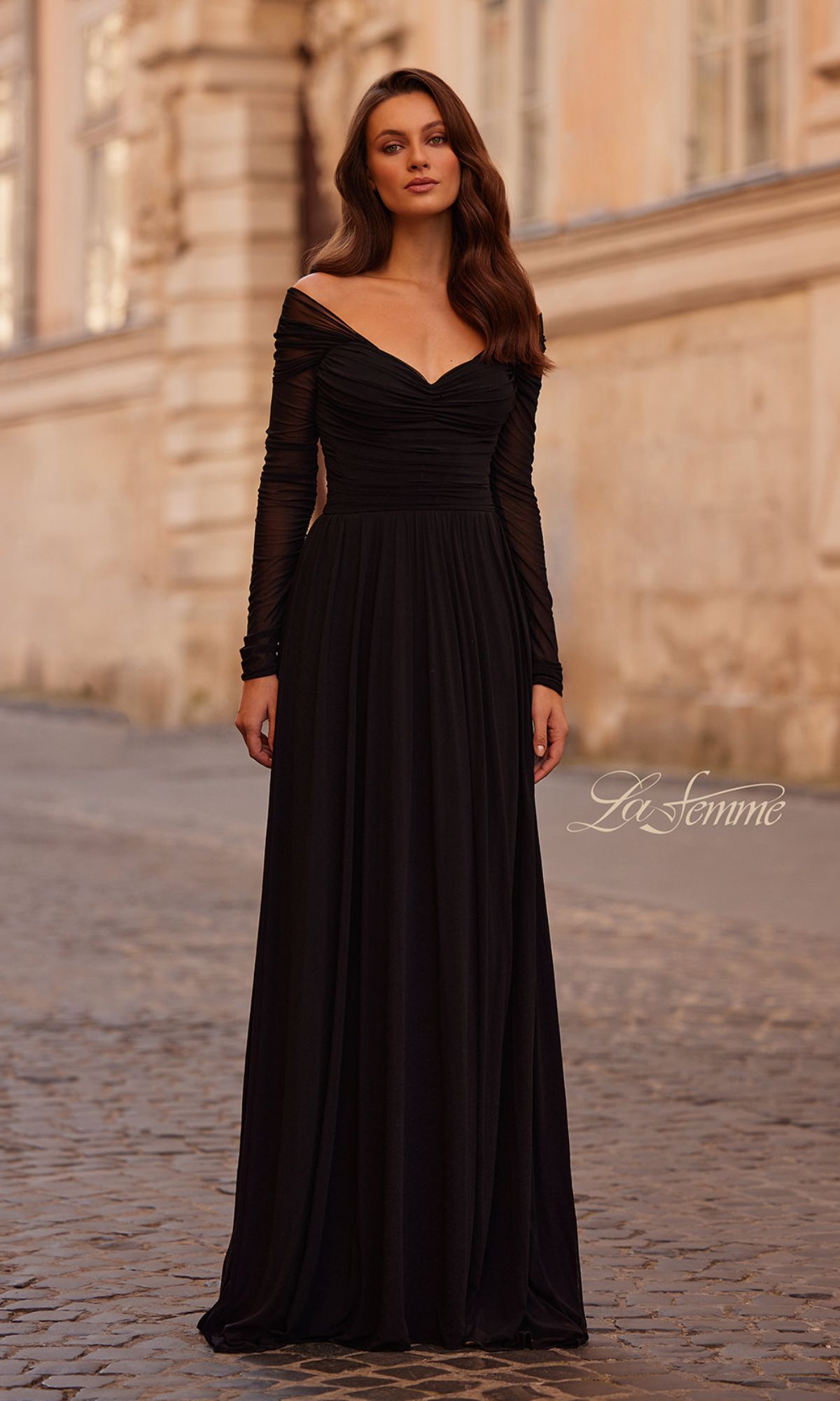 A woman stands on a cobblestone street in the La Femme 32722—an elegant long sleeve black formal dress.