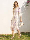 A woman in the Social Queen 3D Floral Embroidered Beaded Dress with a matching purse walks on grass beside a white wall in sunlight.