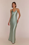 Woman wearing a subtly seductive and effortlessly cool the Brooklyn slip dress  in sage green satin against a beige background