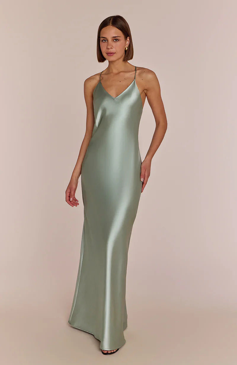 Woman wearing a subtly seductive and effortlessly cool the Brooklyn slip dress  in sage green satin against a beige background