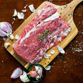 Kentucky grass-fed rose veal brisket on wooden cutting board with garlic, onion, and herbs