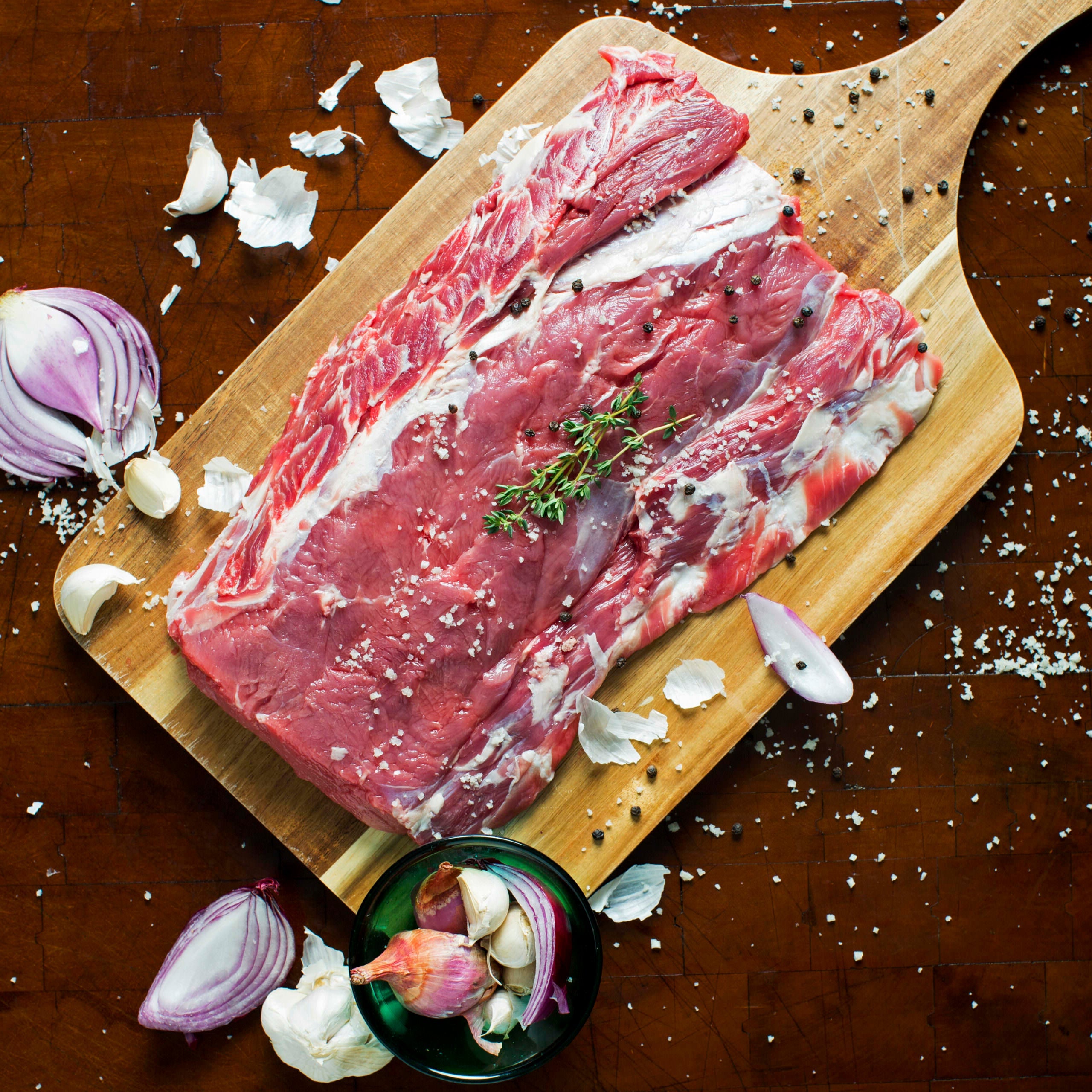 Kentucky grass-fed rose veal brisket on wooden cutting board with garlic, onion, and herbs