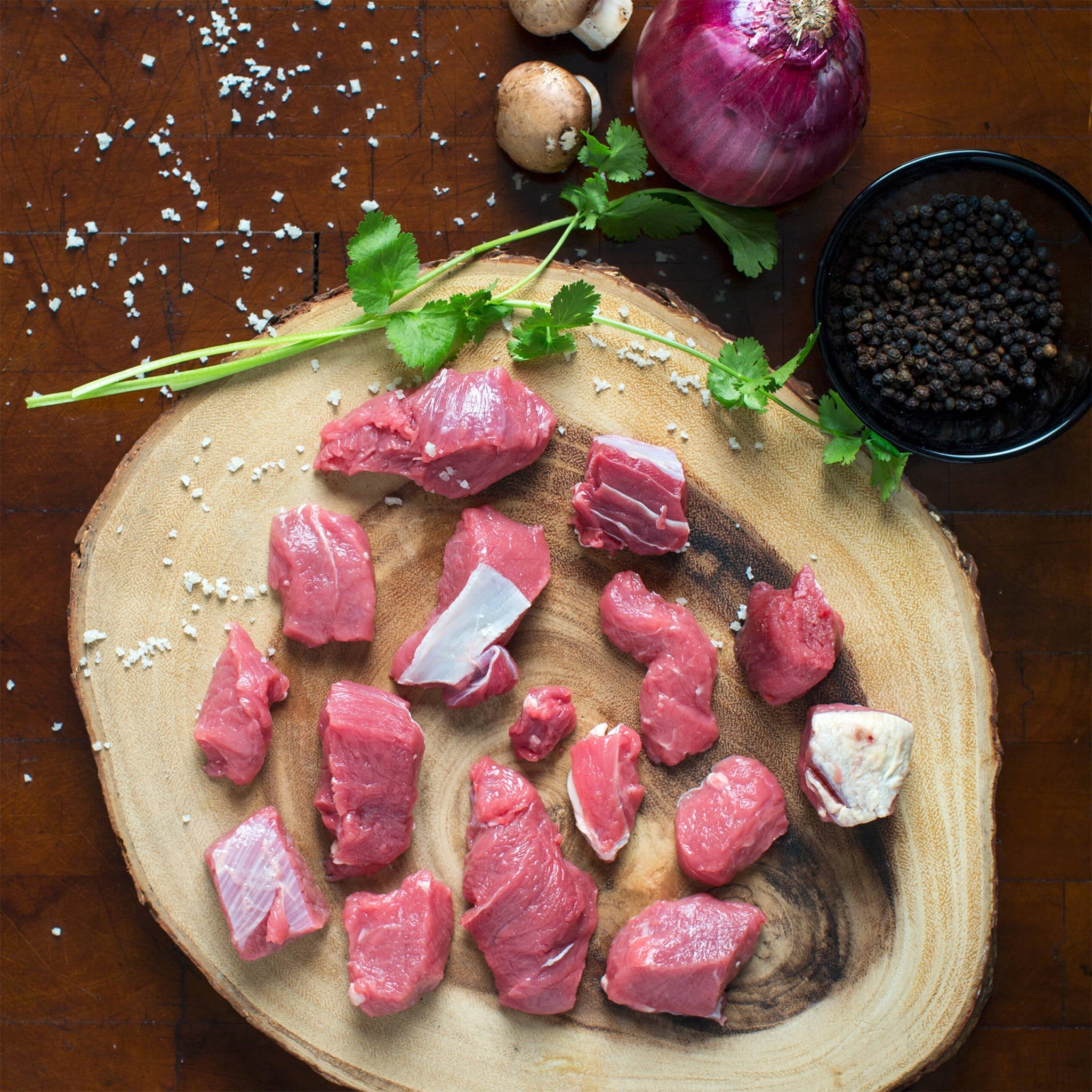 Kentucky grass-fed rose veal stew meat on wooden board with onion, mushrooms, peppercorns, and herbs