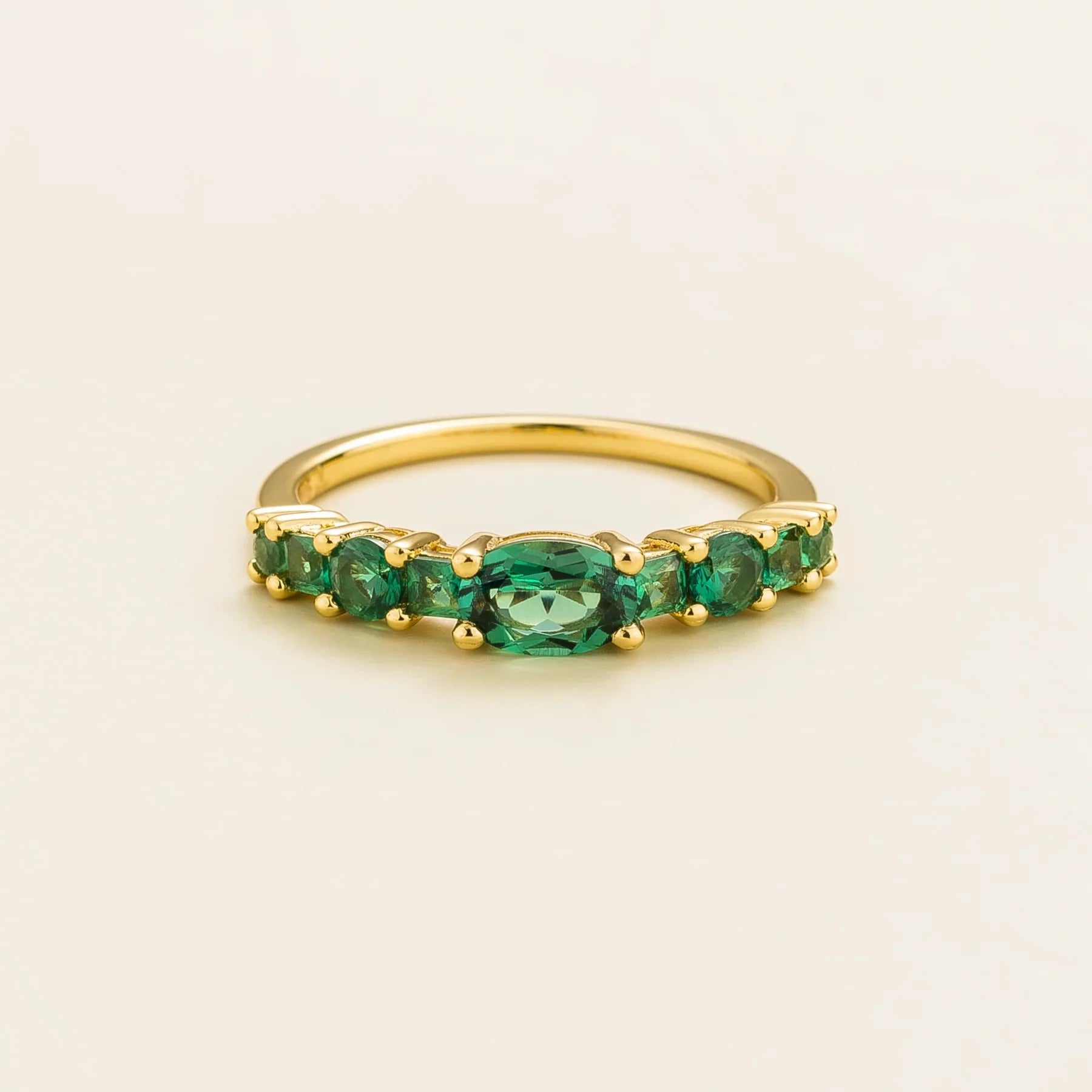 Juvetti yellow gold ring featuring lab-grown emeralds in oval, princess, and round cuts for a timeless half-eternity look.