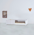 A white wooden toddler floor bed with partial vertical-slat safety rails, styled with floral bedding in a minimalist room.
