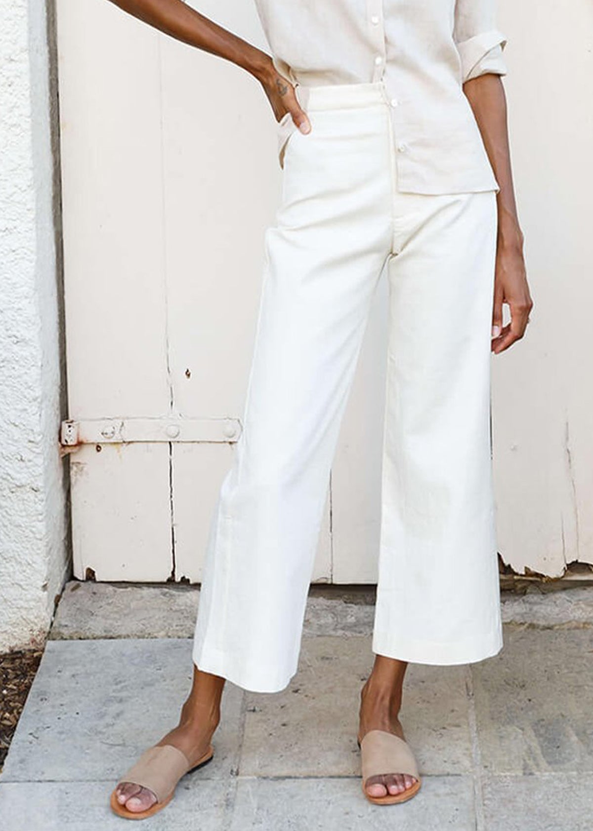 woman wearing white high-waisted, wide-leg pants with a slight ankle crop, single button front closure, and back pockets.